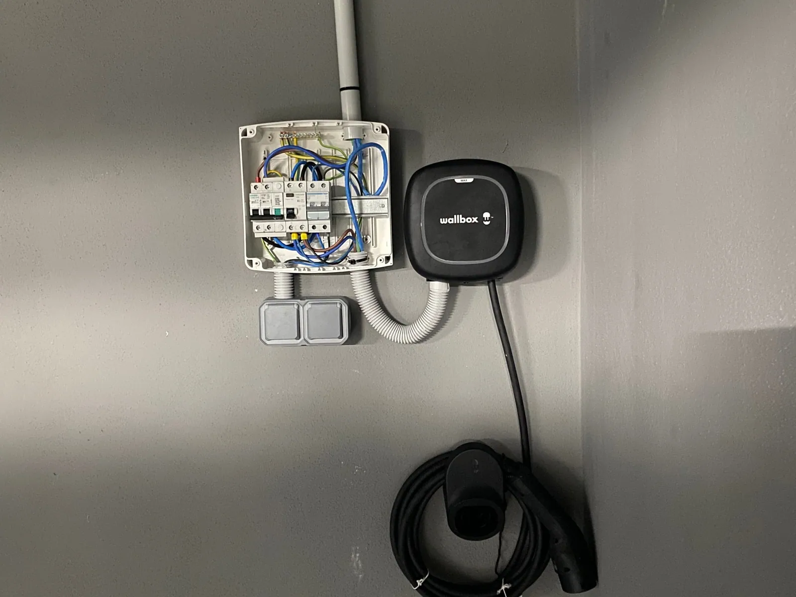 Cargador de coche eléctrico Wallbox instalado junto a su caja de protecciones, con el cable Tipo 2 recogido