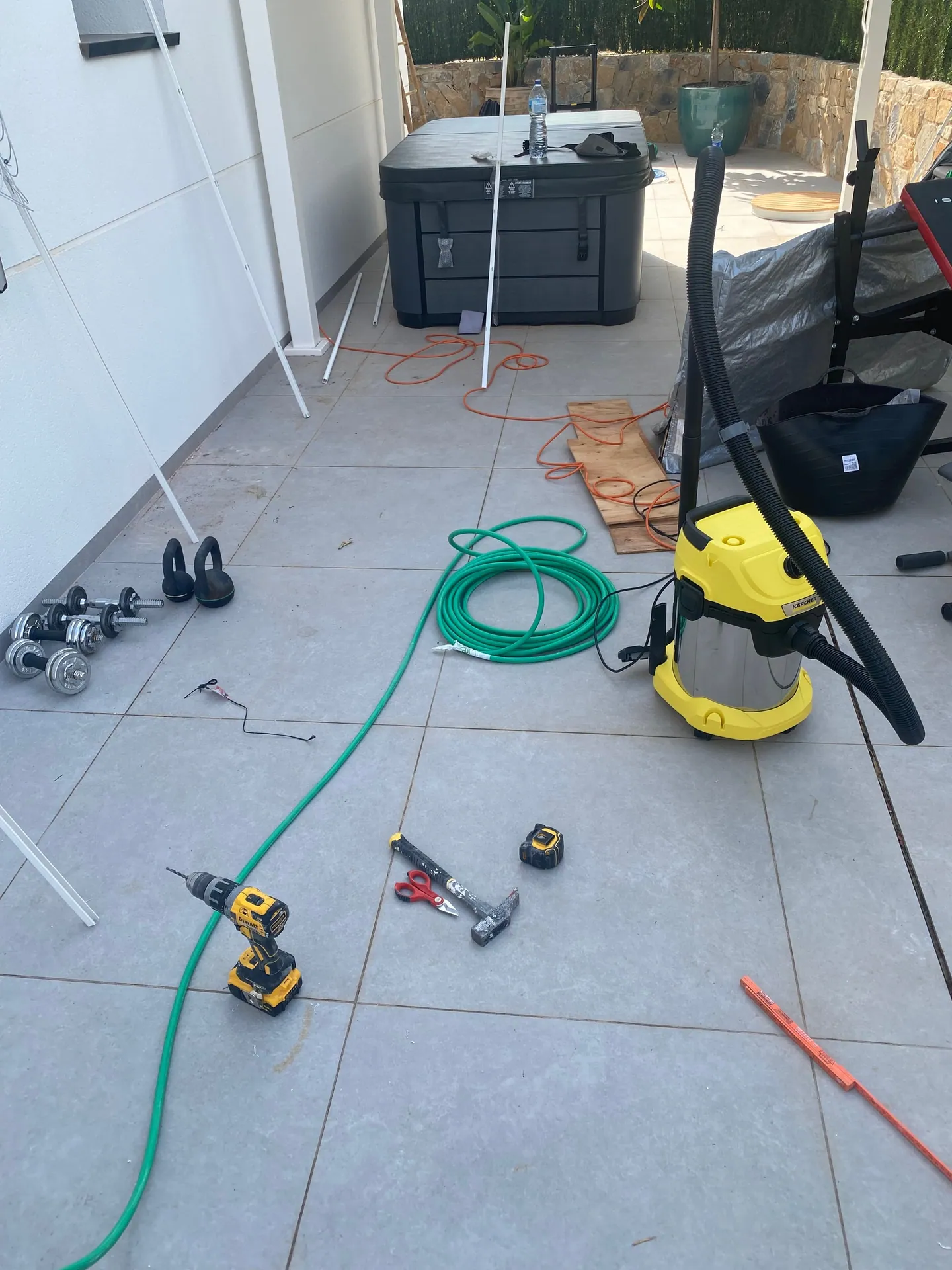 Taladro, martillo y manguera sobre el pavimento de una terraza, con el spa todavía embalado al fondo