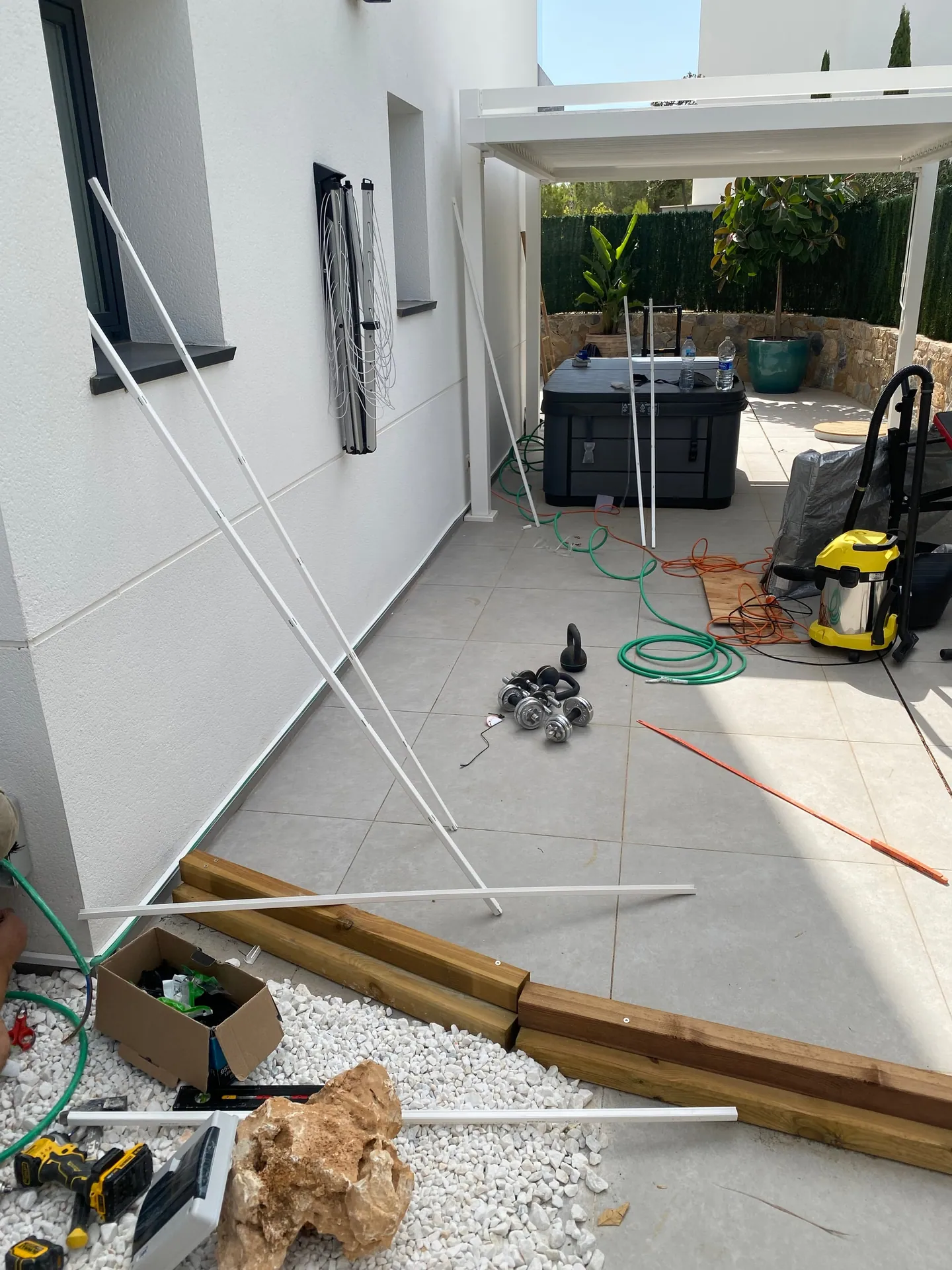 Terraza en obra con perfiles blancos apoyados en la pared, el spa embalado y herramienta repartida